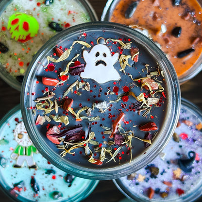 A black Halloween candle with a spooky ghost, orange crystals, and autumn leaves.