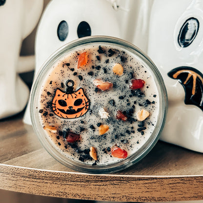 A vintage Halloween candle that is decorated with a spooky retro cat charm, witchy crystals, and spooky glitter.