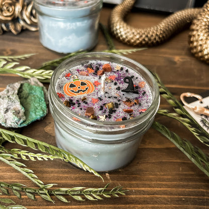 A Halloween candle that is decorated with a jack o lantern, a witch hat, spooky crystals, and autumn glitter.