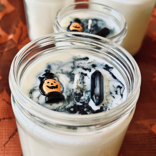 A white Halloween candle with black swirls. The candle is decorated with a spooky jack o lantern and a black obsidian crystal.