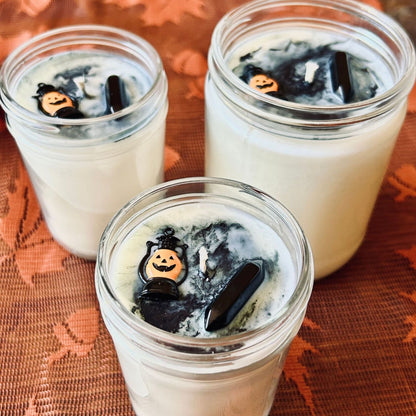 A white Halloween candle with black swirls. The candle is decorated with a spooky jack o lantern and a black obsidian crystal.