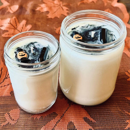 A white Halloween candle with black swirls. The candle is decorated with a spooky jack o lantern and a black obsidian crystal.