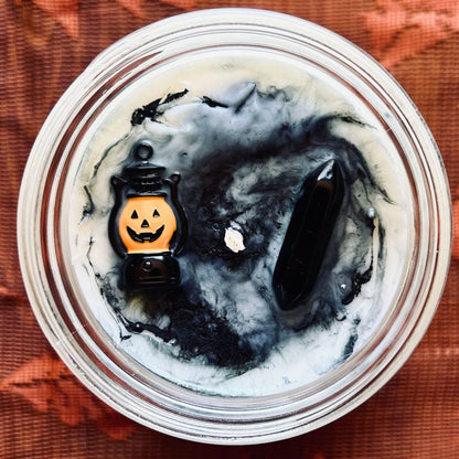 A white Halloween candle with black swirls. The candle is decorated with a spooky jack o lantern and a black obsidian crystal.