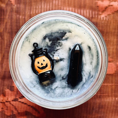 A white Halloween candle with black swirls. The candle is decorated with a spooky jack o lantern and a black obsidian crystal.