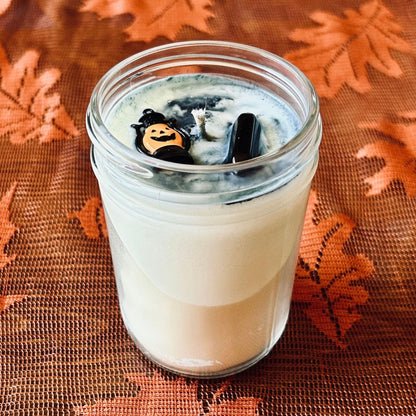 A white Halloween candle with black swirls. The candle is decorated with a spooky jack o lantern and a black obsidian crystal.