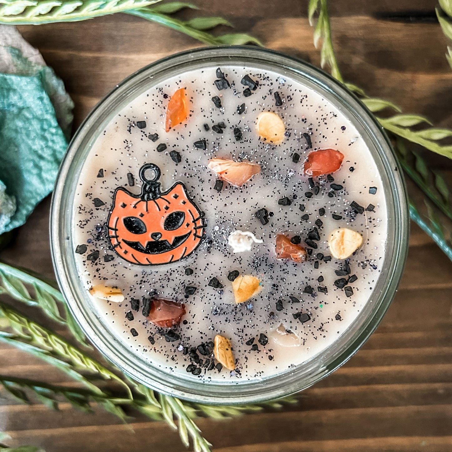 A vintage Halloween candle that is decorated with a spooky retro cat charm, witchy crystals, and spooky glitter.