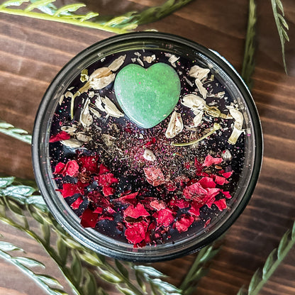 Black intention candle that is decorated with a green aventurine crystal heart. The candle also has jasmine, rose petals, witch hazel, and magic glitter for manifesting.