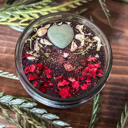 Black intention candle that is decorated with a green aventurine crystal heart. The candle also has jasmine, rose petals, witch hazel, and magic glitter for manifesting.