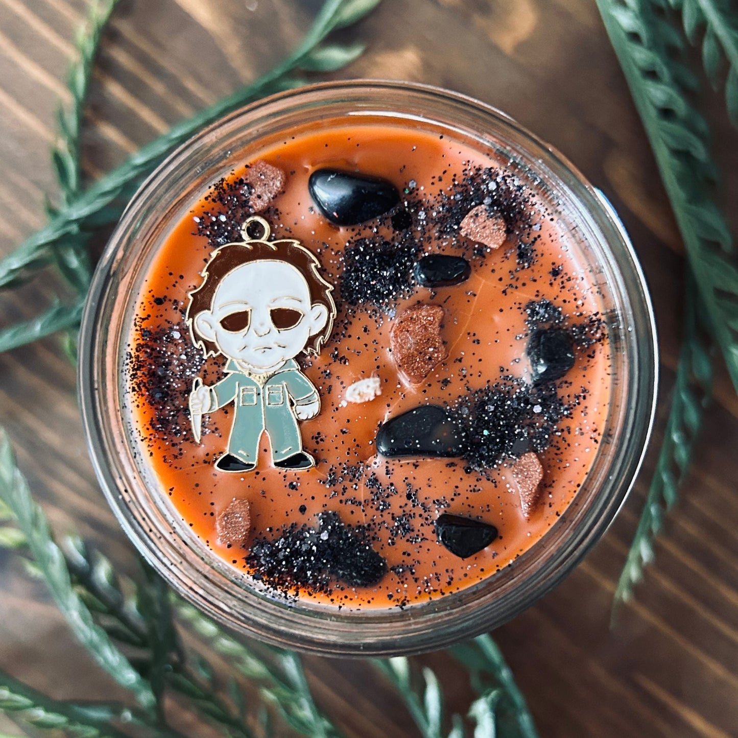 An Orange Halloween candle that is decorated with a Michael Myers horror movie character, spooky crystals, and creepy glitter.