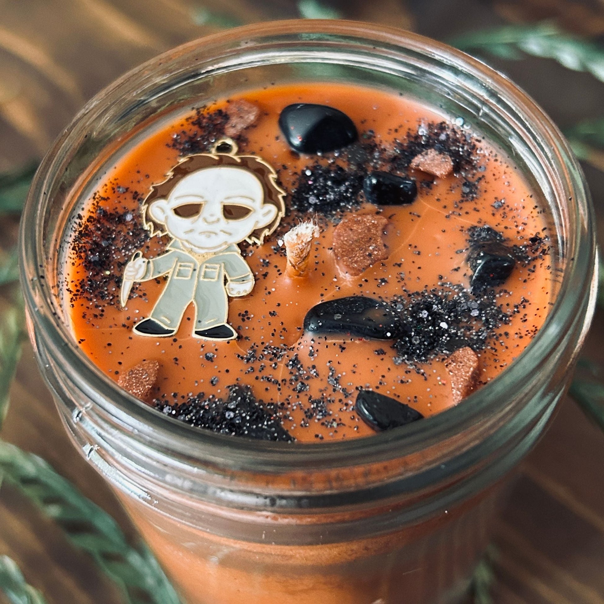 An Orange Halloween candle that is decorated with a Michael Myers horror movie character, spooky crystals, and creepy glitter.