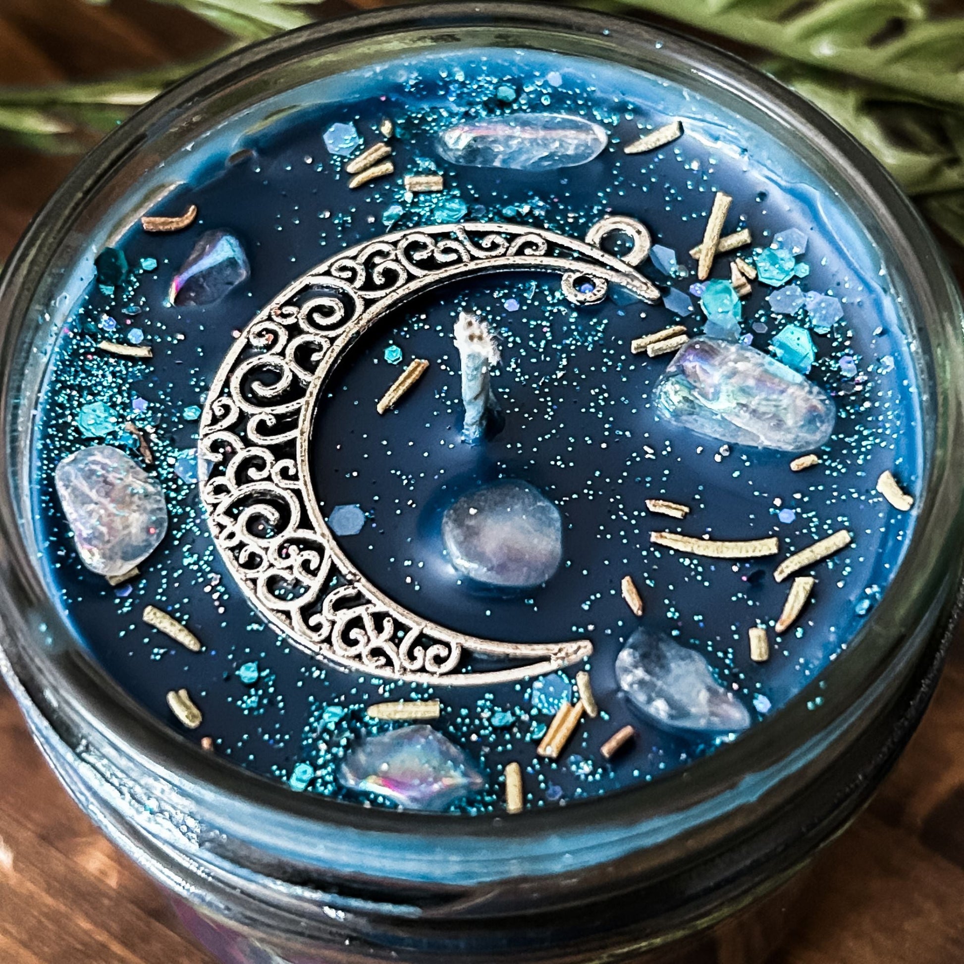 Blue intention candle that is decorated with a silver crescent moon. The candle also has rosemary, aura quartz crystals, and celestial glitter for moon ritual spells and manifesting.