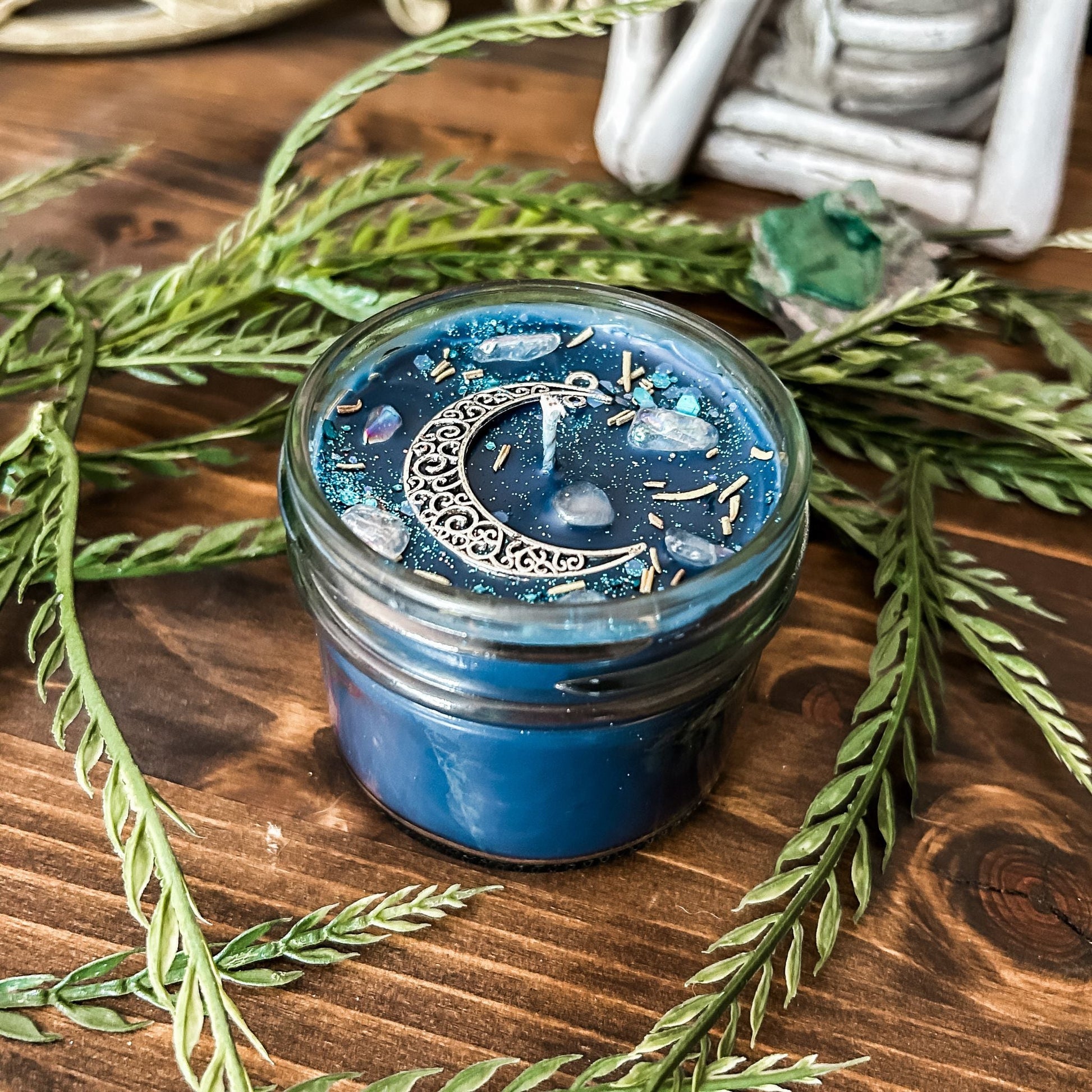 Blue intention candle that is decorated with a silver crescent moon. The candle also has rosemary, aura quartz crystals, and celestial glitter for moon ritual spells and manifesting.