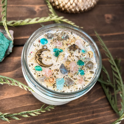 White intention candle that is decorated with a mystical crescent moon. The candle also has crystals, herbs, and magic glitter for setting intentions for new beginnings and fresh starts.