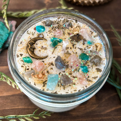 White intention candle that is decorated with a mystical crescent moon. The candle also has crystals, herbs, and magic glitter for setting intentions for new beginnings and fresh starts.