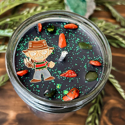 A black Halloween candle that is decorated with a horror movie charm, spooky crystals, and gothic glitter.