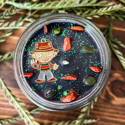 A black Halloween candle that is decorated with a horror movie charm, spooky crystals, and gothic glitter.