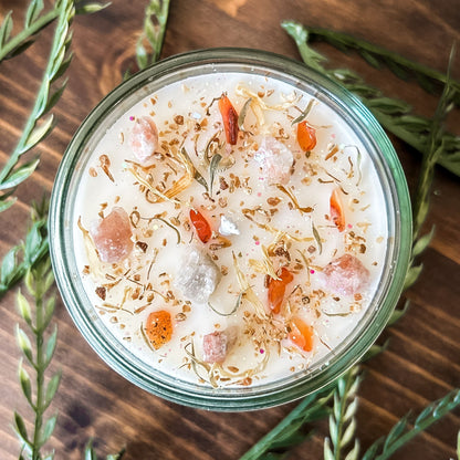 White crystal intention candle that is decorated with witchy crystals, herbs, and glitter for positive energy, healing energy, and cleansing.