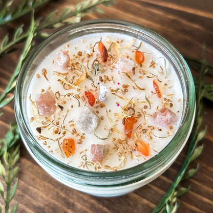 White crystal intention candle that is decorated with witchy crystals, herbs, and glitter for positive energy, healing energy, and cleansing.