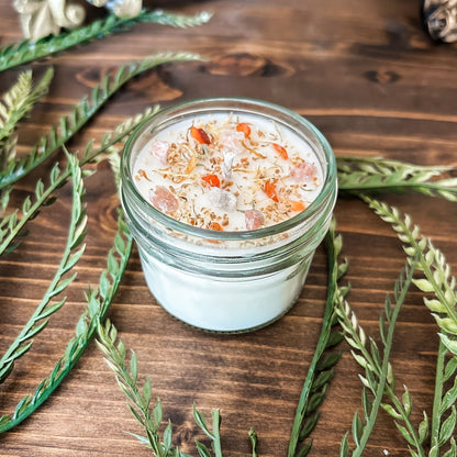 White crystal intention candle that is decorated with witchy crystals, herbs, and glitter for positive energy, healing energy, and cleansing.