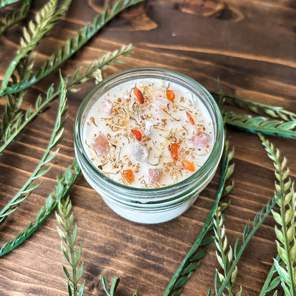 White crystal intention candle that is decorated with witchy crystals, herbs, and glitter for positive energy, healing energy, and cleansing.