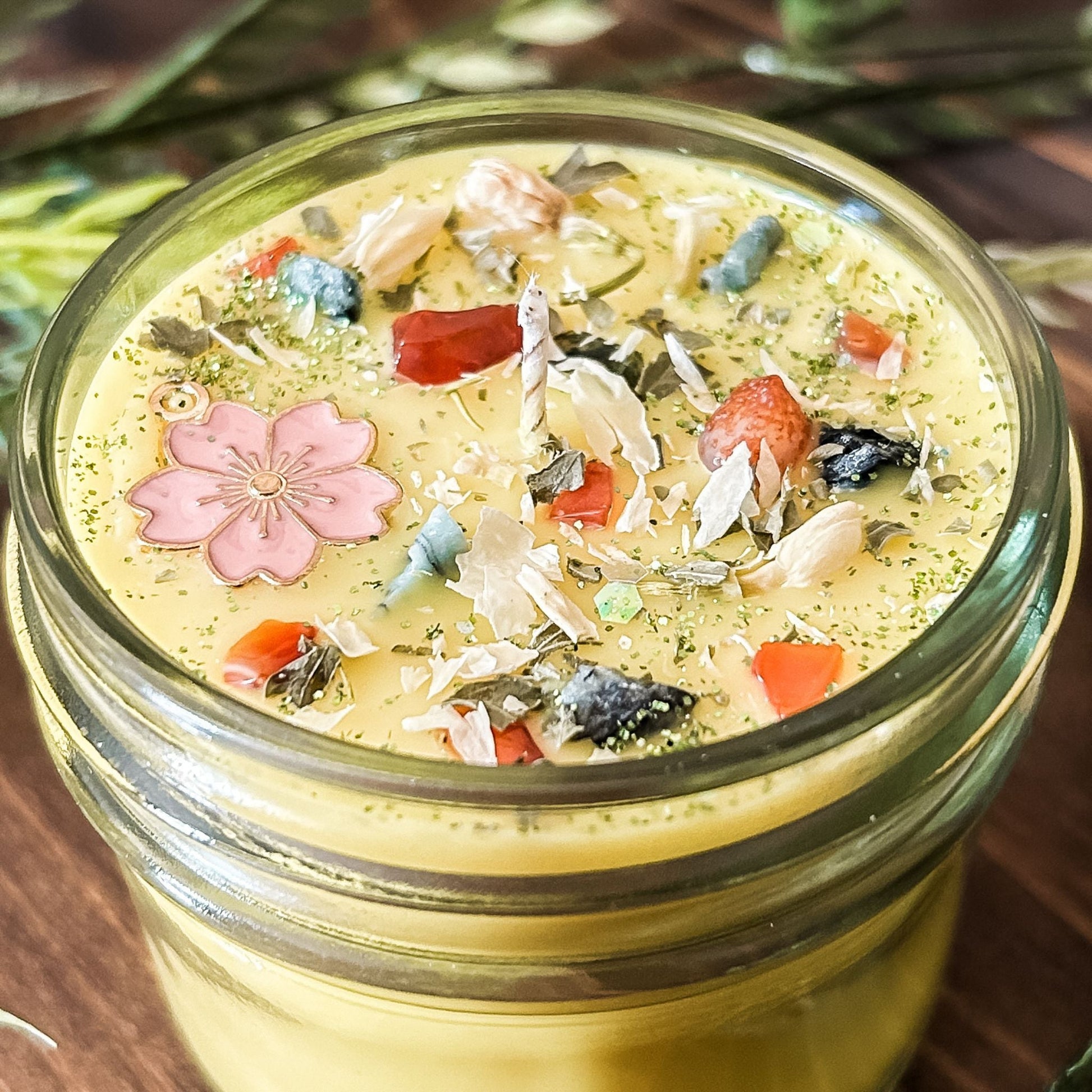 yellow intention pagan candle that is decorated with a pink flower, crystals, flowers, and magic glitter. The candle represents Beltane and is for setting intentions for renewal, positive energy, purity, and fertility.