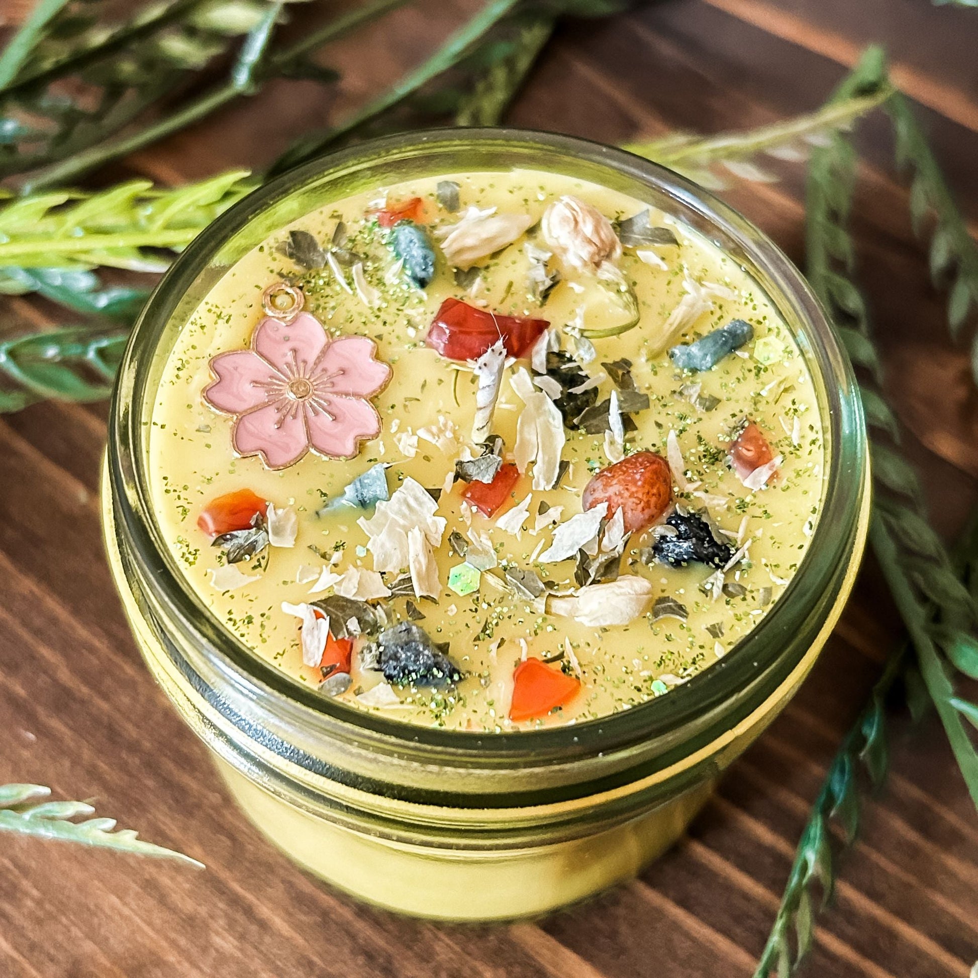yellow intention pagan candle that is decorated with a pink flower, crystals, flowers, and magic glitter. The candle represents Beltane and is for setting intentions for renewal, positive energy, purity, and fertility.