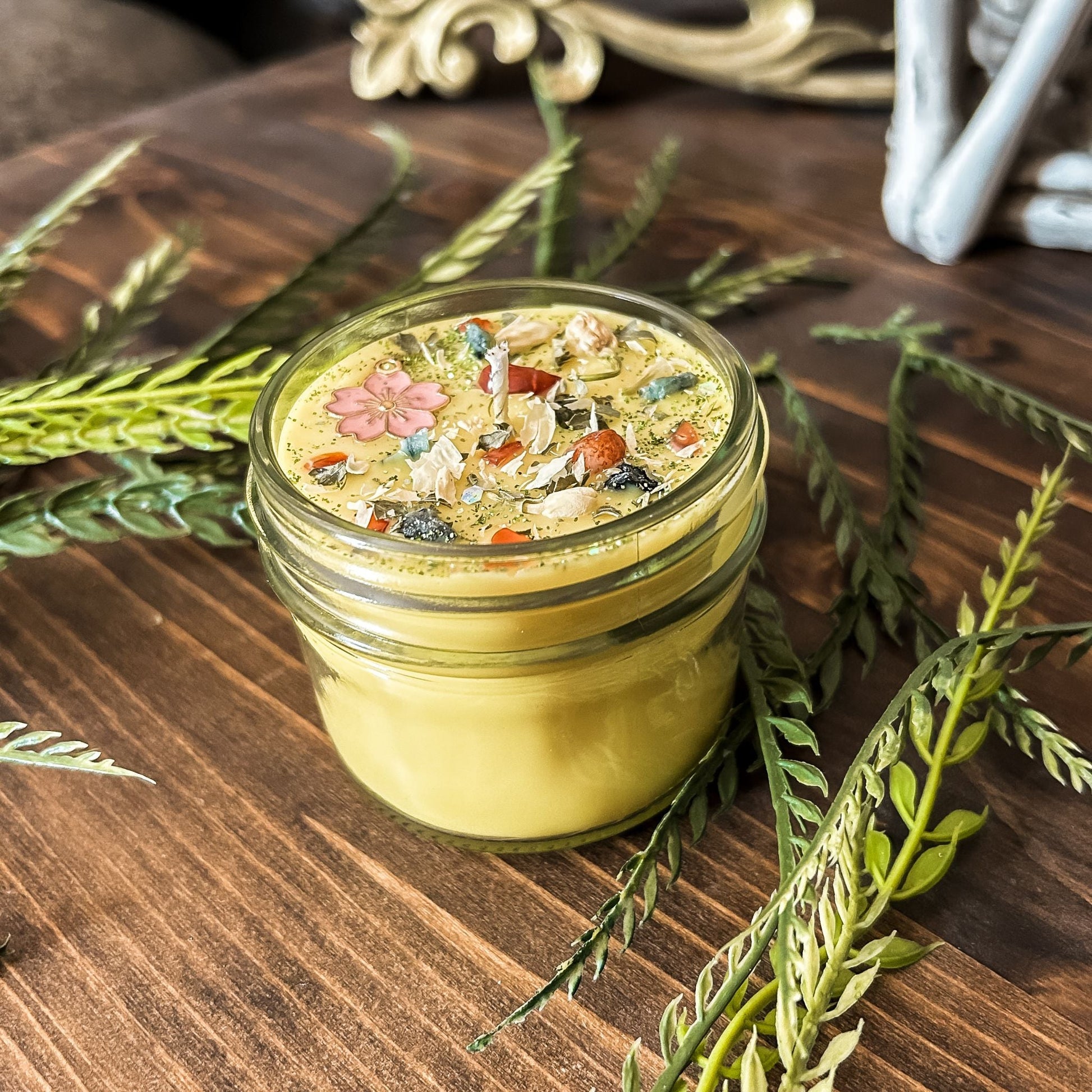 yellow intention pagan candle that is decorated with a pink flower, crystals, flowers, and magic glitter. The candle represents Beltane and is for setting intentions for renewal, positive energy, purity, and fertility.