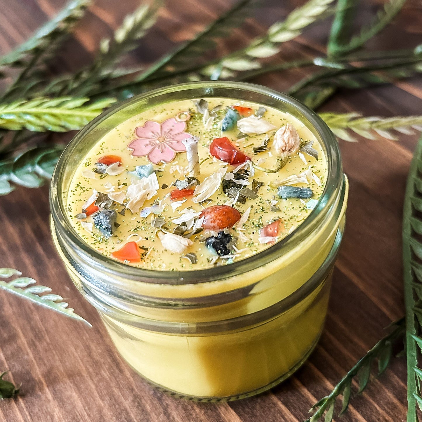 yellow intention pagan candle that is decorated with a pink flower, crystals, flowers, and magic glitter. The candle represents Beltane and is for setting intentions for renewal, positive energy, purity, and fertility.
