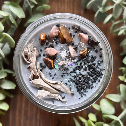 Silver intention candle that is decorated with gold tigers eye crystal, smokey quartz crystal, rhodonite crystal, protection salt, white sage, and witchy glitter to manifest goddess energy and power.