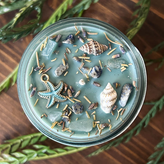 Seafoam green intention candle that is decorated with a starfish, seashells, herbs, and witchy glitter for sea witch work and ocean magic rituals.
