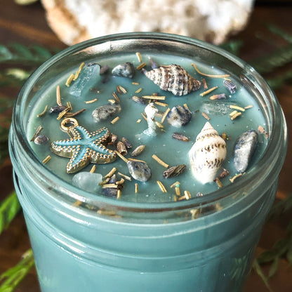 Seafoam green intention candle that is decorated with a starfish, seashells, herbs, and witchy glitter for sea witch work and ocean magic rituals.
