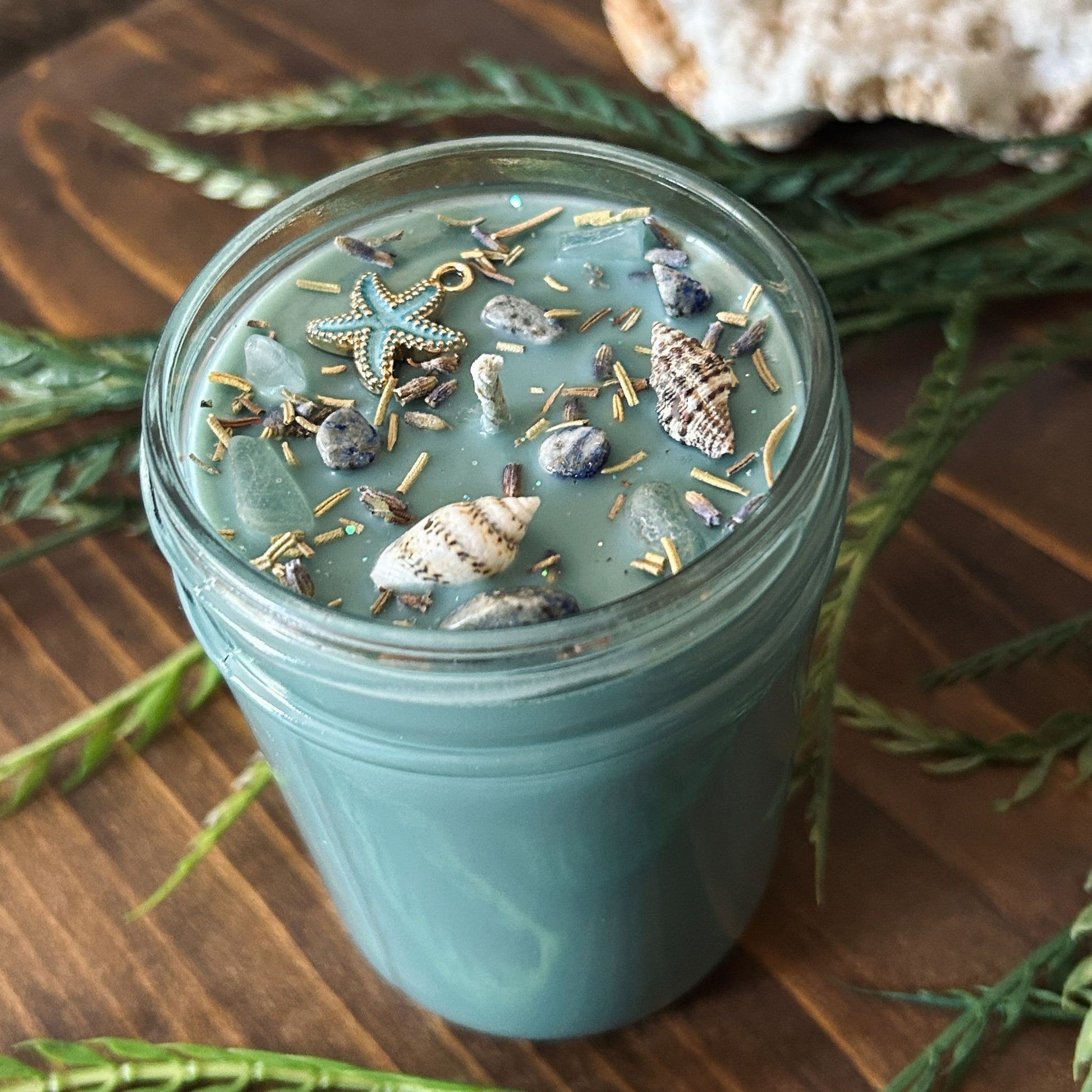 Seafoam green intention candle that is decorated with a starfish, seashells, herbs, and witchy glitter for sea witch work and ocean magic rituals.