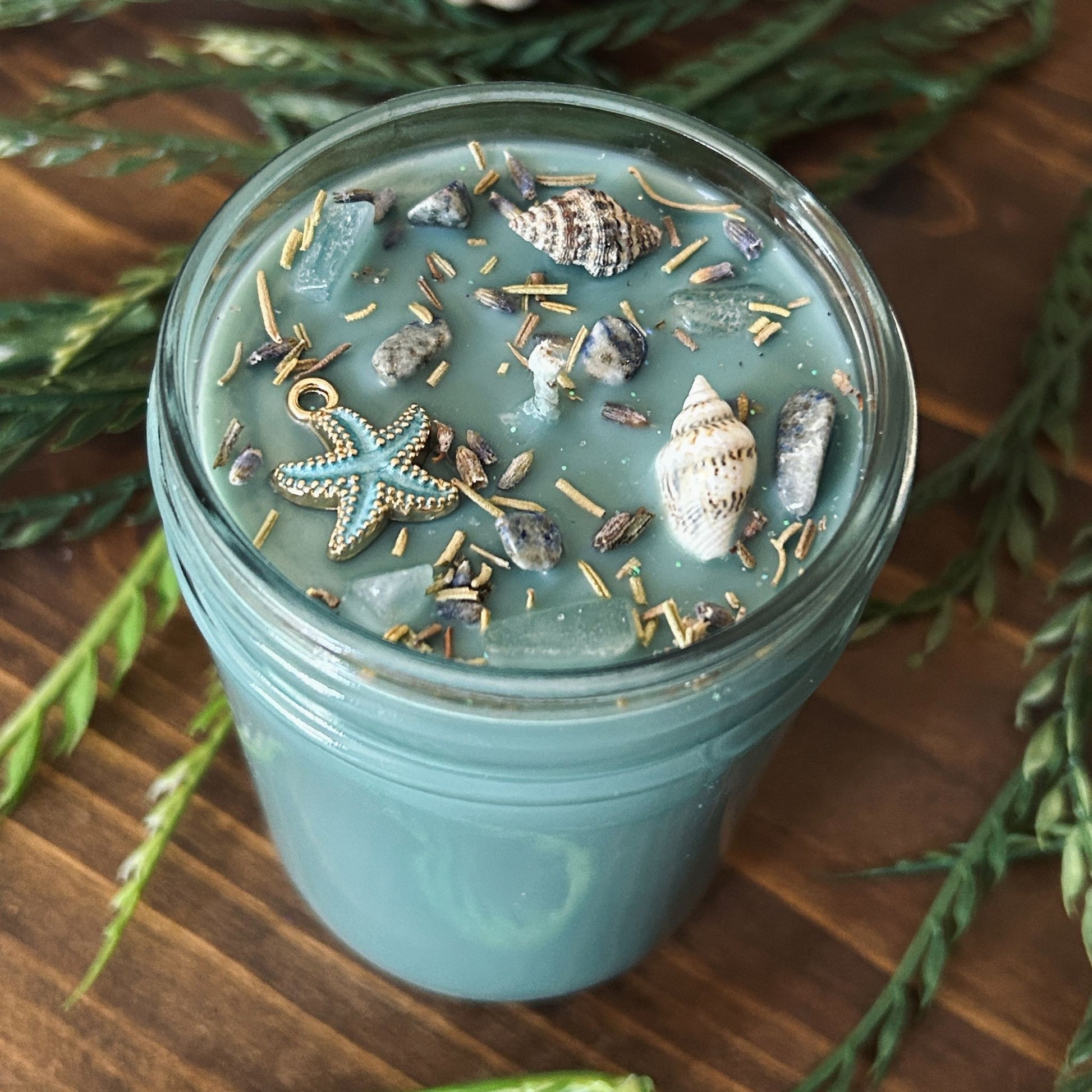 Seafoam green intention candle that is decorated with a starfish, seashells, herbs, and witchy glitter for sea witch work and ocean magic rituals.