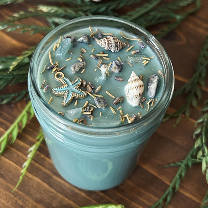 Seafoam green intention candle that is decorated with a starfish, seashells, herbs, and witchy glitter for sea witch work and ocean magic rituals.