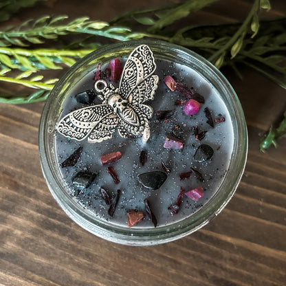 A gothic gray candle that is decorated with a gothic moth, spooky pink crystals, and dark glitter.