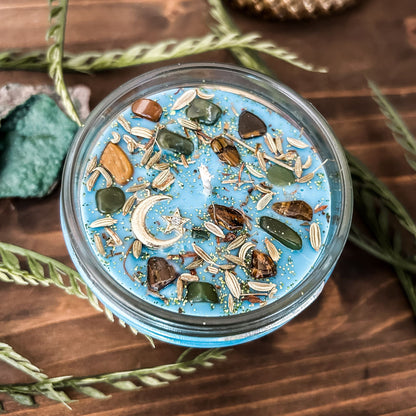 Light blue intention Litha candle that is decorated with crystals, flowers, and magic glitter to celebrate summer solstice. The candle is decorated to represent abundance, growth, nature, and pagan rituals.