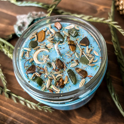 Light blue intention Litha candle that is decorated with crystals, flowers, and magic glitter to celebrate summer solstice. The candle is decorated to represent abundance, growth, nature, and pagan rituals.