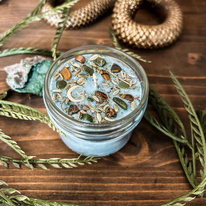 Light blue intention Litha candle that is decorated with crystals, flowers, and magic glitter to celebrate summer solstice. The candle is decorated to represent abundance, growth, nature, and pagan rituals.