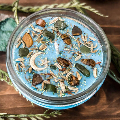 Light blue intention Litha candle that is decorated with crystals, flowers, and magic glitter to celebrate summer solstice. The candle is decorated to represent abundance, growth, nature, and pagan rituals.
