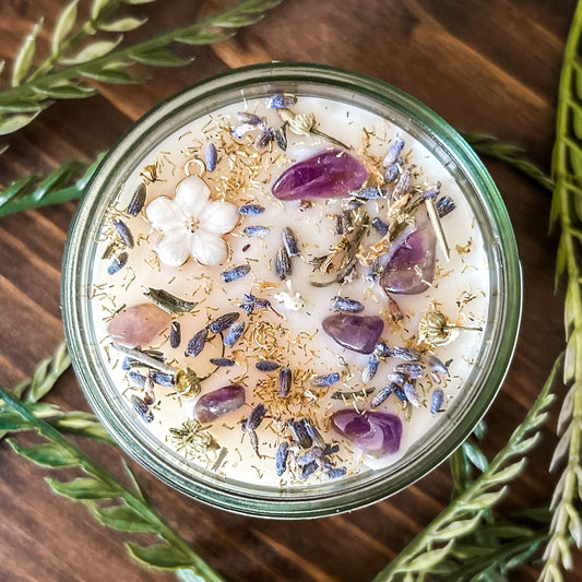 Natural soy intention candle that is decorated with a white flower, amethyst crystals. lavender, chamomile, and glitter for healing, anxiety relief, and calm energy.