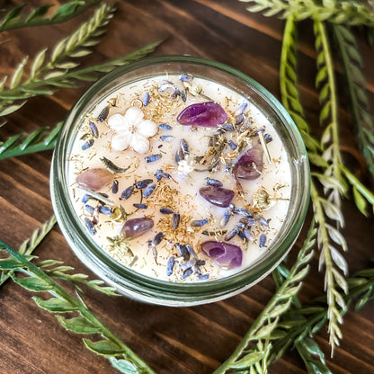 Natural soy intention candle that is decorated with a white flower, amethyst crystals. lavender, chamomile, and glitter for healing, anxiety relief, and calm energy.