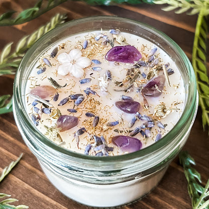Natural soy intention candle that is decorated with a white flower, amethyst crystals. lavender, chamomile, and glitter for healing, anxiety relief, and calm energy.