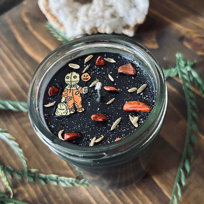 A black Halloween candle decorated with a spooky horror movie charm, witchy crystals, and gothic glitter.