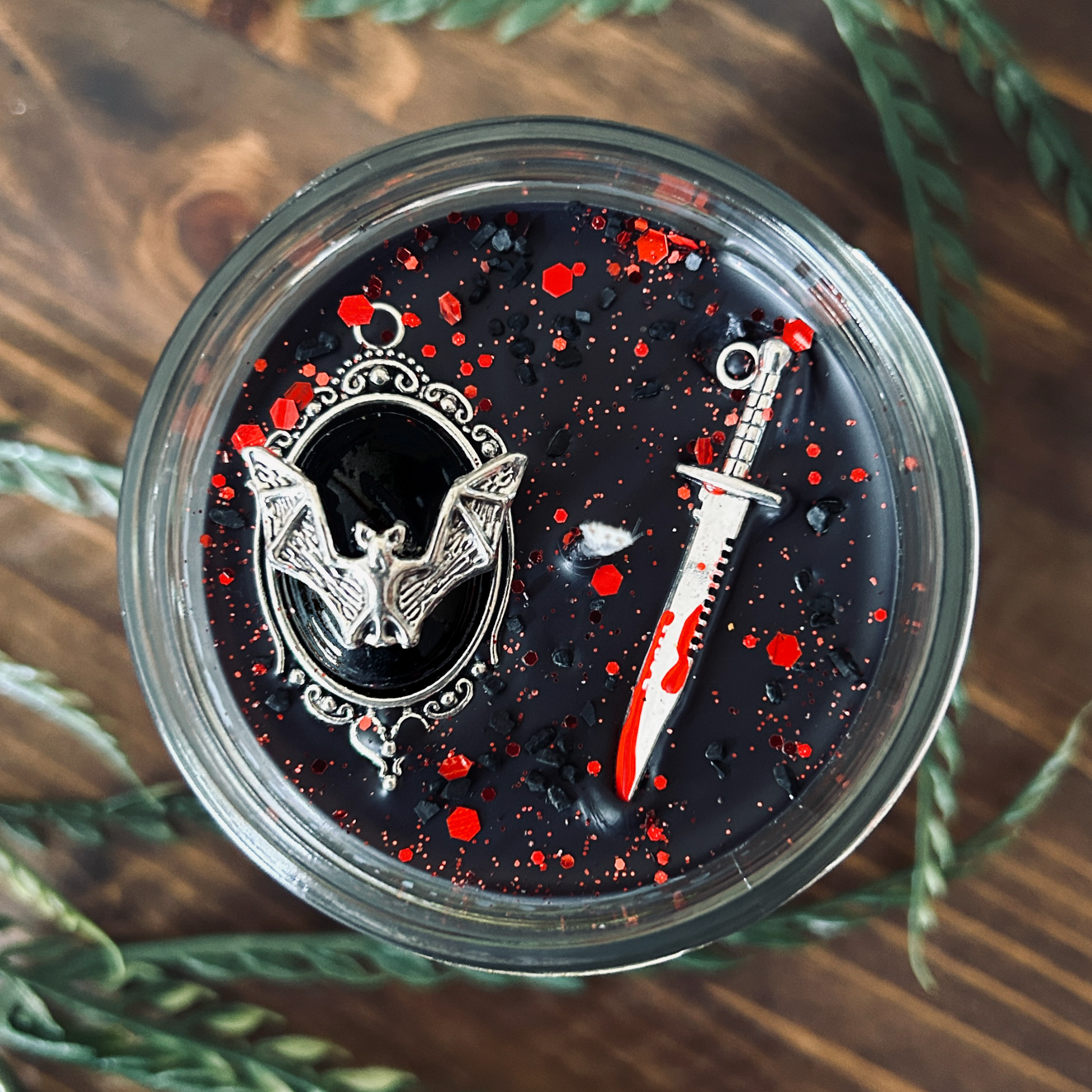 A black gothic candle that is decorated with a spooky bat, a bloody dagger, and gothic red glitter.
