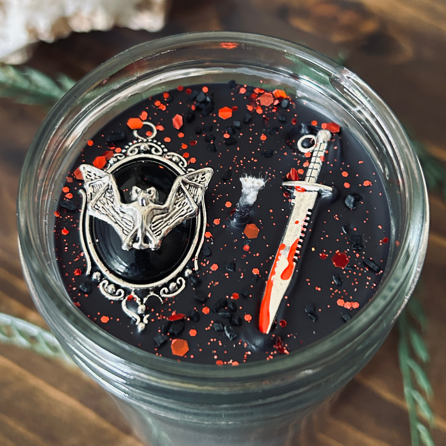 A black gothic candle that is decorated with a spooky bat, a bloody dagger, and gothic red glitter.