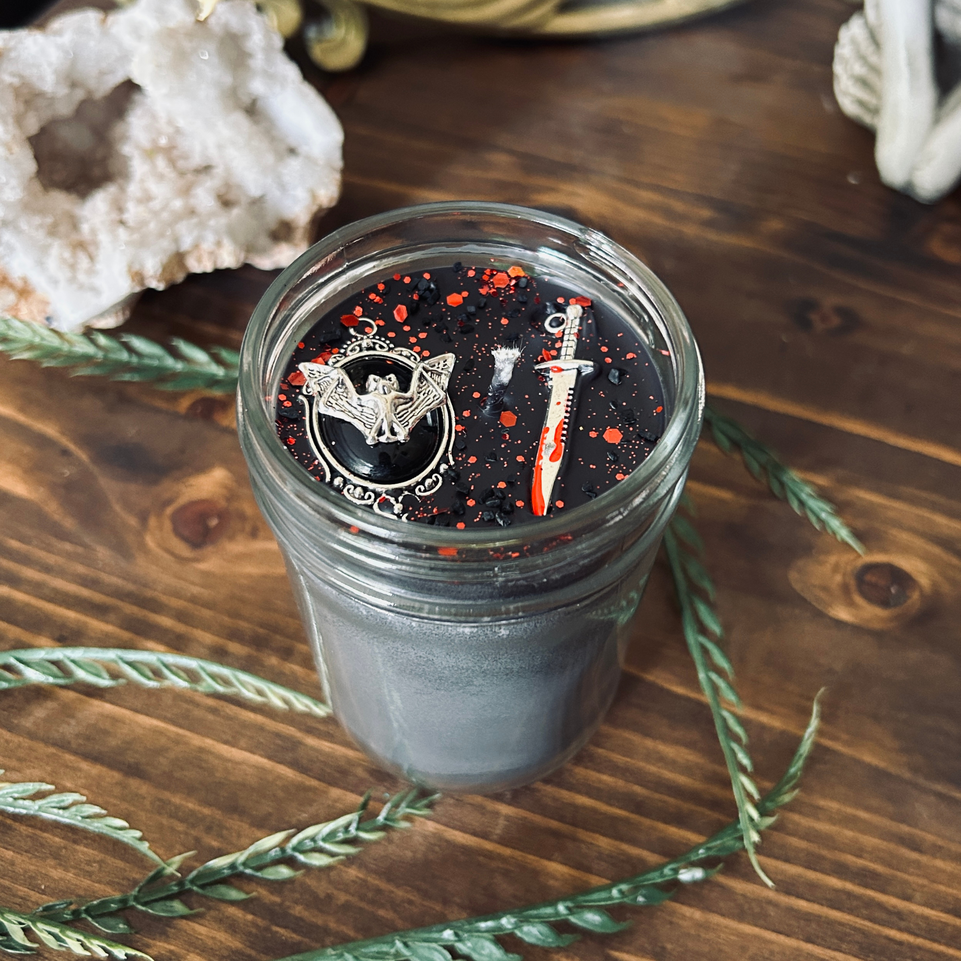 A black gothic candle that is decorated with a spooky bat, a bloody dagger, and gothic red glitter.