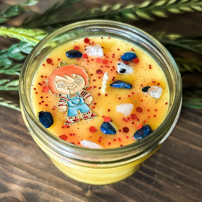 A yellow Halloween candle that is decorated with a horror movie chucky charm, spooky crystals, and creepy glitter.