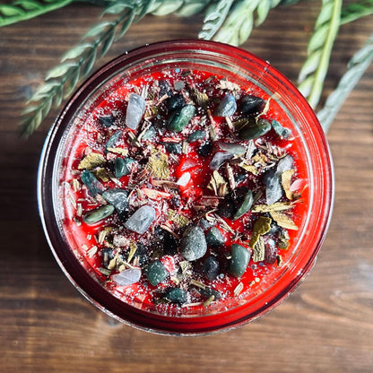 Red intention pagan candle that is decorated with witchy crystals, flowers, and magic glitter to represent Winter Solstice and Yule.