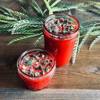 Red intention pagan candle that is decorated with witchy crystals, flowers, and magic glitter to represent Winter Solstice and Yule.