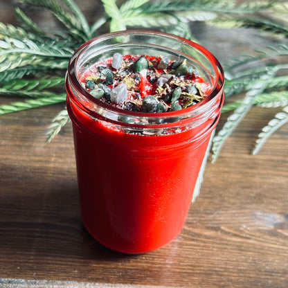 Red intention pagan candle that is decorated with witchy crystals, flowers, and magic glitter to represent Winter Solstice and Yule.